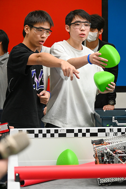 Two PAS VEX Robotics team members compete passionately during the PAS VEX Signature Event 2024, showcasing teamwork and strategy with their robot and game elements.